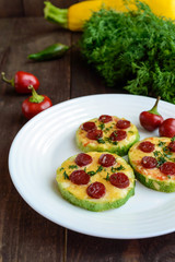 Small zucchini pizza on the circles with pepperoni and mozzarella. On a dark wooden background.