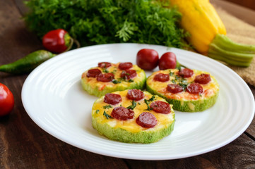 Small zucchini pizza on the circles with pepperoni and mozzarella. On a dark wooden background.