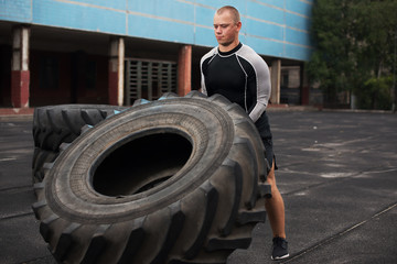 Fototapeta na wymiar Man raises a big tire on the artificial field