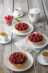 A weathered wood table with raspberry chocolate tarts and tea. Bright sun lit room. 