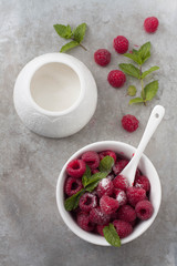 Fresh ripe raspberries in a white bowl, Sugar bowl and more berries on a gray background. 