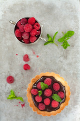 Chocolate tart with fresh raspberries and mint leaves, gray background 