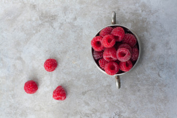 Red fresh raspberries in a vintage pewter bowl. Minimalist, gray background. 