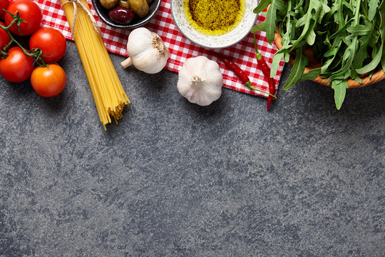 Italian food ingredients background with raw spaghetti, olives, rocket salad, garlic, olive oil and tomatoes.