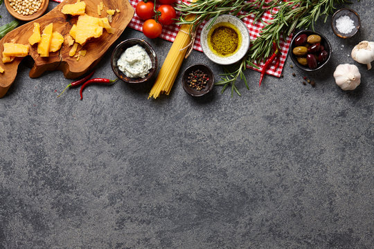 Italian food ingredients background with raw spaghetti, olives, basil leaves, rosemary, parmesan cheese, ricotta, garlic, chili pepper, pine nuts, olive oil and tomatoes.