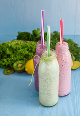 Fototapeta na wymiar healthy food concept. colorful milkshakes in glass and fresh green vegetables on blue wooden desk