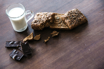Bread with seeds, chocolate and cup of milk on the table.