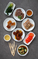 Assorted Asian appetizers on white plates:  octopus in spicy sauce, sliced beef shank, pigs ears, crispy barbecue pork . Dark gray background 