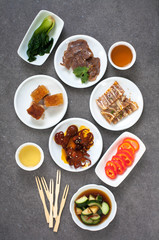 Assorted Asian appetizers on white plates:  octopus in spicy sauce, sliced beef shank, pigs ears, crispy barbecue pork . Dark gray background 