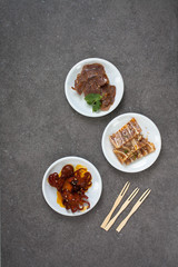 Assorted Asian appetizers on white plates:  octopus in spicy sauce, sliced beef shank, pigs ears, crispy barbecue pork . Dark gray background 