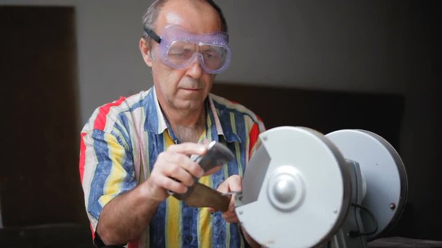 Sharpening axe using a grinding machine. Man sharpens the ax protective glasses