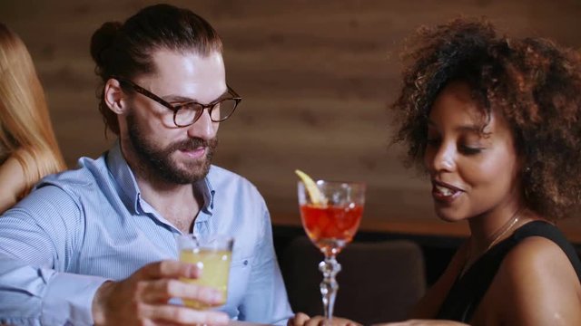 Hipster with a black beard flirts with a very beautiful cheerful black fancy woman in a luxury bar. They drinks cocktailsand chatting