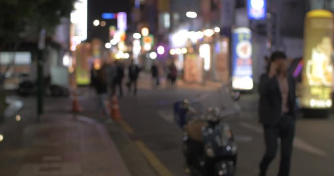 Defocused shot of night street with walking people, illuminated store banners and parked motorbike in Seoul, South Korea. Faces and logos unidentified