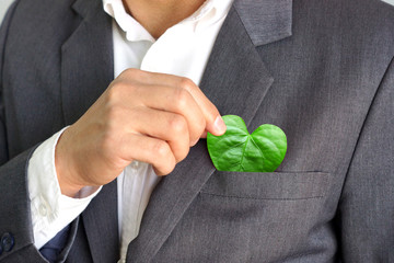 Businessman holding a green heart leaf / Business with corporate social responsibility and...