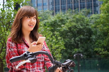 Young Japanese woman using smartphone (cell phone) riding on a bike in a city