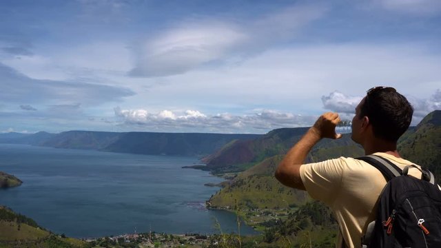 Male traveler drinking water and looking at Toba lake in North Sumatra, Indonesia. Young man living active life