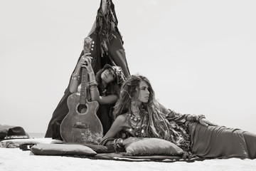 Two beautiful gypsy girls with guitar on pillows at tepee