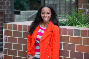 Happy beautiful african american woman wearing red jacket standing and smiling at student college campus.