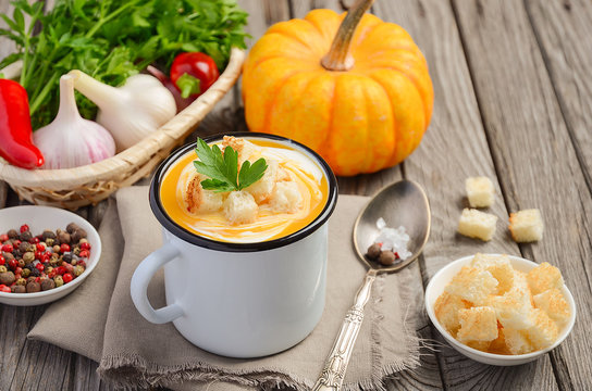 Pumpkin soup with cream and parsley in a mug on wooden background, selective focus