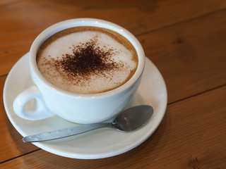 Cappuccino coffee in white cup on wooden table.