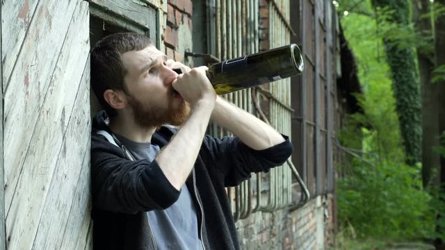 Man drinking wine while talking on cellphone next to the abandoned building
