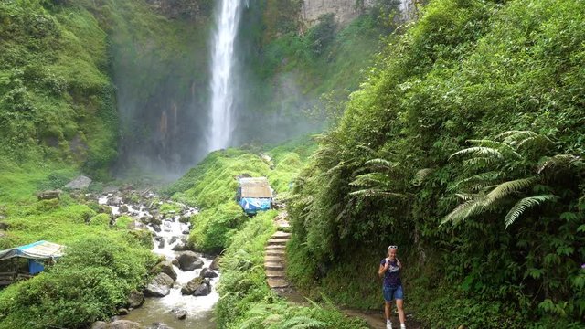 Young woman backpacker walking towards beautiful Sipiso-Piso waterfall on North Sumatra, Indonesia