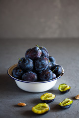Plums in a bowl on a gray background and half plums and plum stones on the table