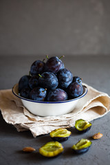 Plums in a bowl on a rural tablecloth on a gray background and half plums and plum stones on the table