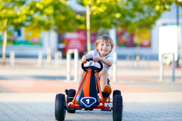 little kid boy driving pedal race car in summer