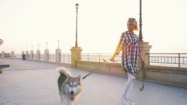 Young female walking with siberian husky dog on sea front at sunrise, slow motion