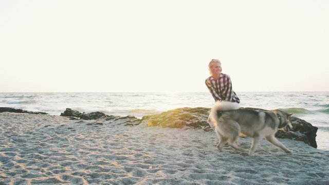 Young female playing with siberian husky dog on the beach at sunrise,slow motion