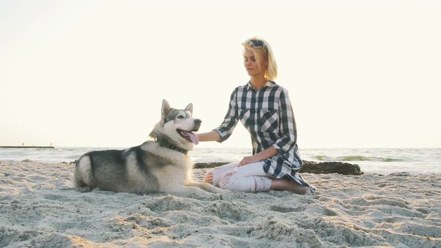 Young female playing with siberian husky dog on the beach at sunrise, slow motion
