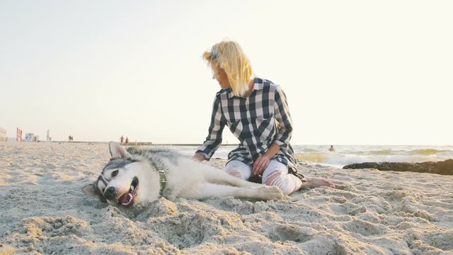 Young female playing with siberian husky dog on the beach at sunrise, slow motion