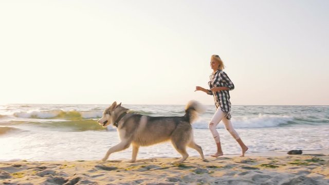 Young female running and playing with siberian husky dog on the beach at sunrise,slow motion