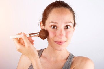 Young attractive woman applying powder wiith brush on her face