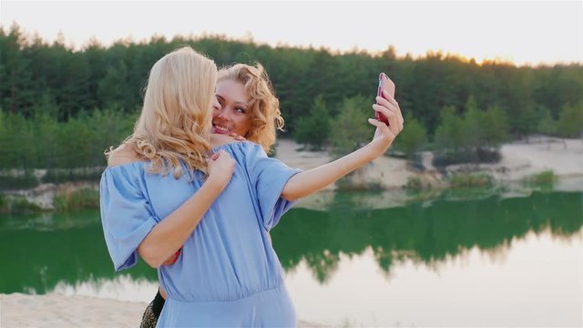 Steadicam shot: Two attractive women in dresses make selfie on the background of the picturesque lakes and forests