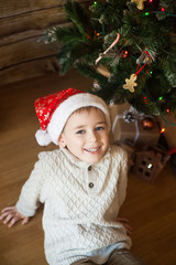 Boy in a Christmas hat in front of decorated tree
