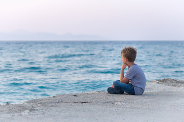 Fototapeta na wymiar Child enjoying the early sunset seascape sitting on a pier