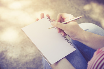 A woman writing something on empty notebook.