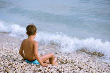 Fototapeta na wymiar child sitting on a pebble beach and watching the waves
