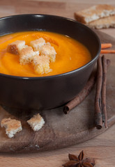 Pumpkin soup in a brown bowl on dark wood