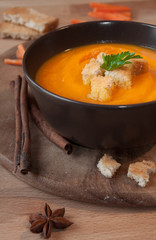 Pumpkin soup in a brown bowl on dark wood