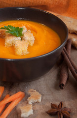 Pumpkin soup in a brown bowl on dark wood