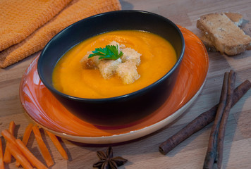 Pumpkin soup in a brown bowl on dark wood