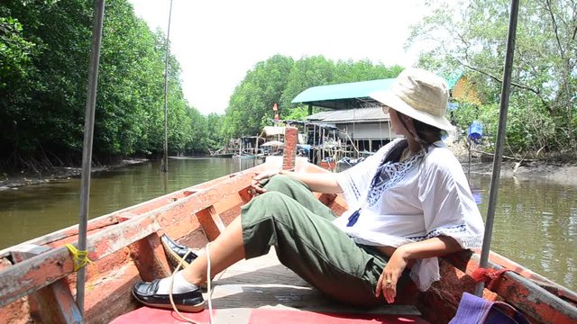 Traveller thai woman sit on service long tail boat for looking and travel view riverbank and Mangroves forest or Intertidal forest on river of Pak Nam Prasae town in Rayong, Thailand.