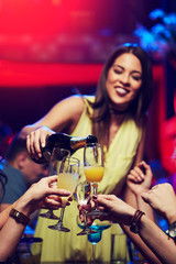 Smiling girl in the club poured champagne to her friends