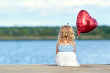 Fotobehang kleines Mädchen sitzt am Steg mit roten Ballon © Jenny Sturm
