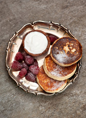 baked cottage cheese pancakes with sour cream and raspberries  on a gray marble background