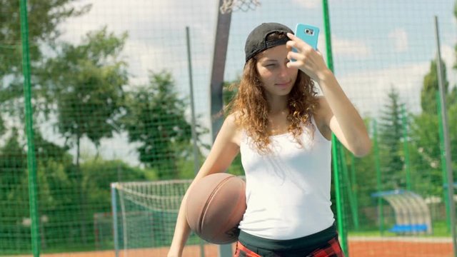 Happy girl holding basketball and doing selfies on smartphone
