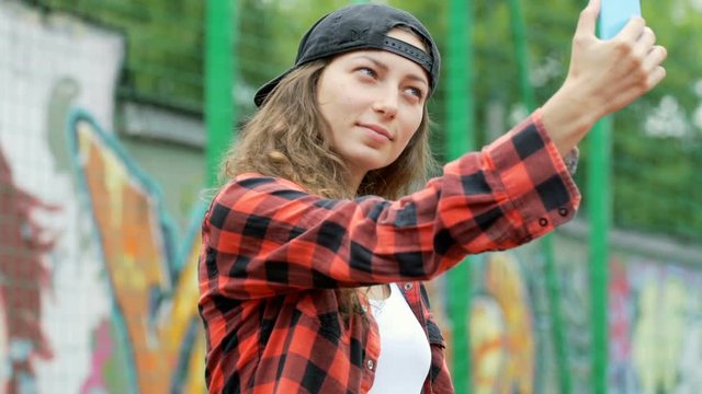 Hipster girl doing selfie on smartphone while standing next to the graffiti
